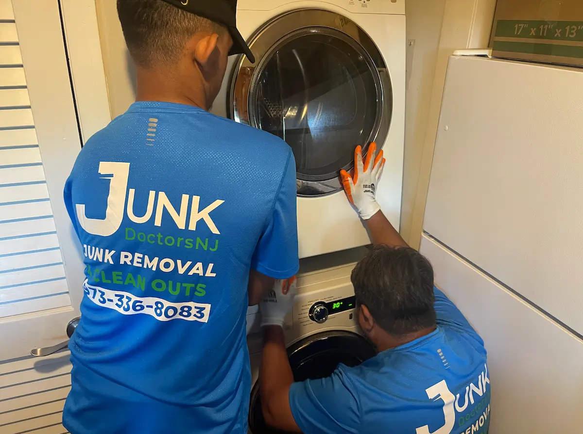Professional junk removal team navigating a tight space to remove a stacked washer and dryer during an apartment cleanout.