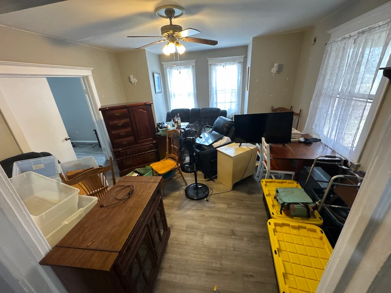 Before photo of a cluttered New Jersey apartment living room filled with a TV, dresser, and various household items.