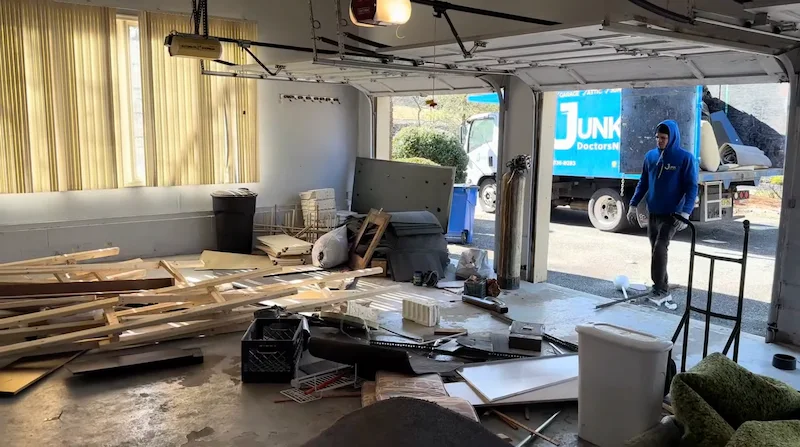 Junk Doctors NJ crew member removing wood scraps and renovation debris from a residential garage during a construction site clearing project.