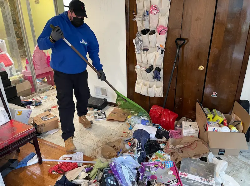 JunkDoctors crew member wearing a mask and gloves while raking up loose trash and debris during an eviction cleanout in New Jersey.