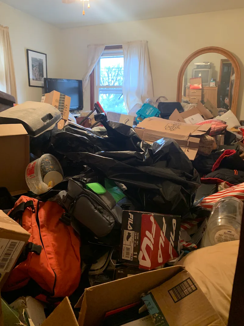 A bedroom in Morristown, New Jersey with extreme hoarding conditions, including piles of boxes, bags, and household items, before a professional cleanout by Junk Doctors.