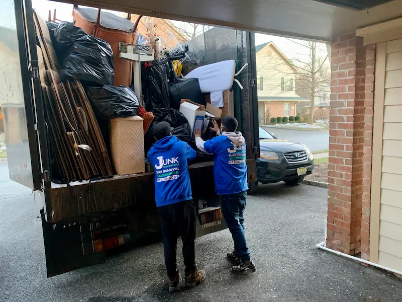 Two JunkDoctors workers efficiently loading a variety of household items and debris into a full truck during a New Jersey garage cleanout.