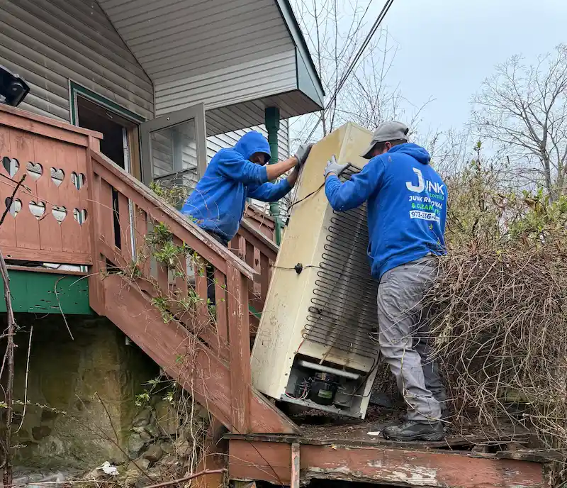 Two Junk Doctors NJ professionals carefully moving a heavy old refrigerator down steep outdoor stairs for disposal and recycling.