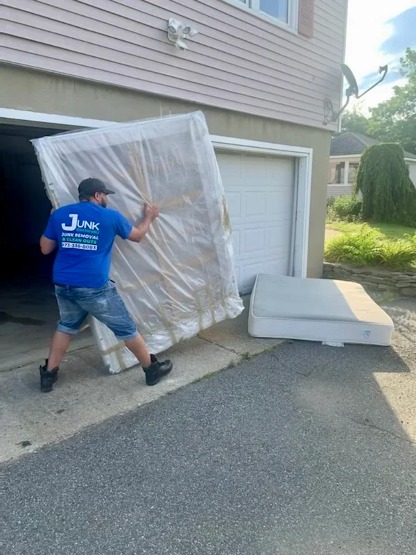 Junk Doctors NJ team member removing a wrapped box spring and mattress from a residential garage for eco-friendly disposal.