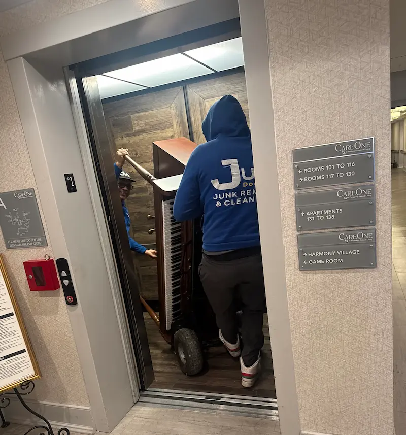 Junk Doctors NJ crew members carefully moving a piano into an elevator for removal at a CareOne senior living facility in North NJ.