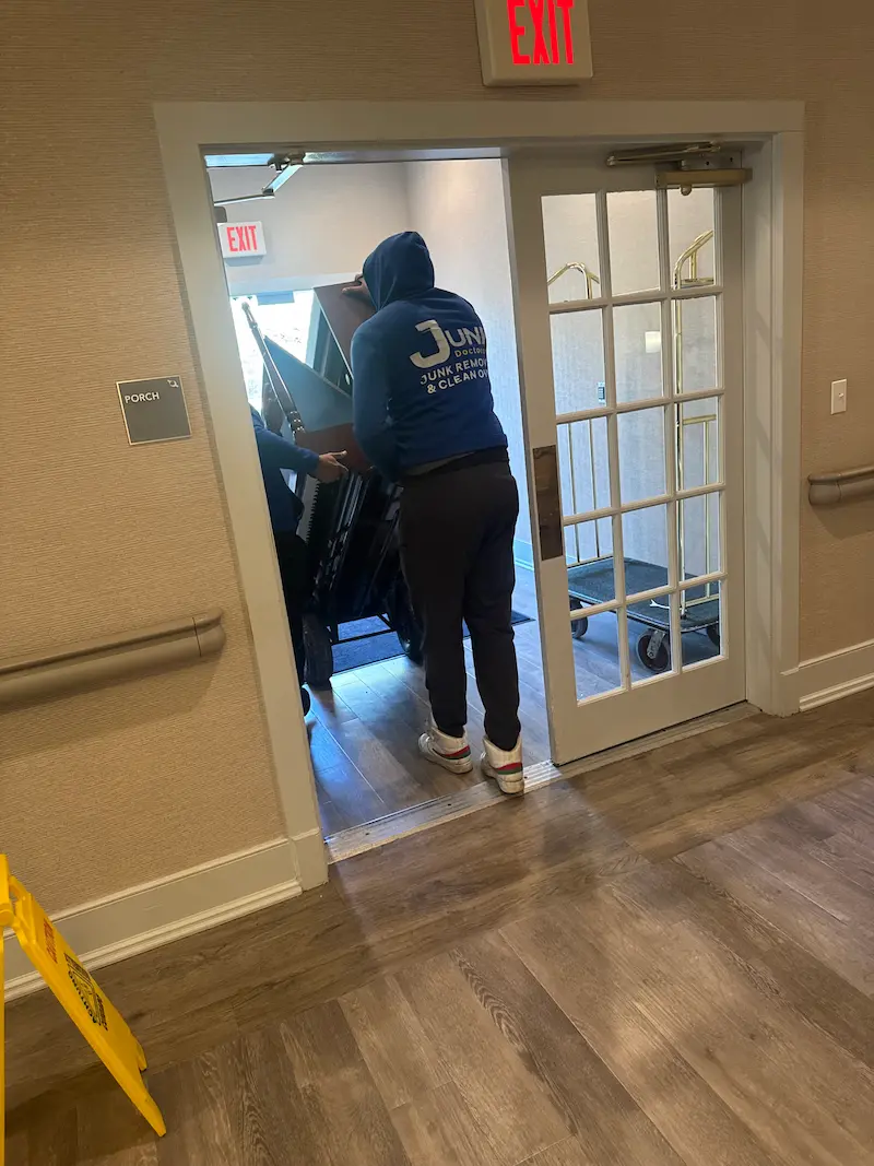 Junk Doctors NJ professionals carefully navigating a piano on a dolly through a doorway during a specialty cleanout service in North Jersey.