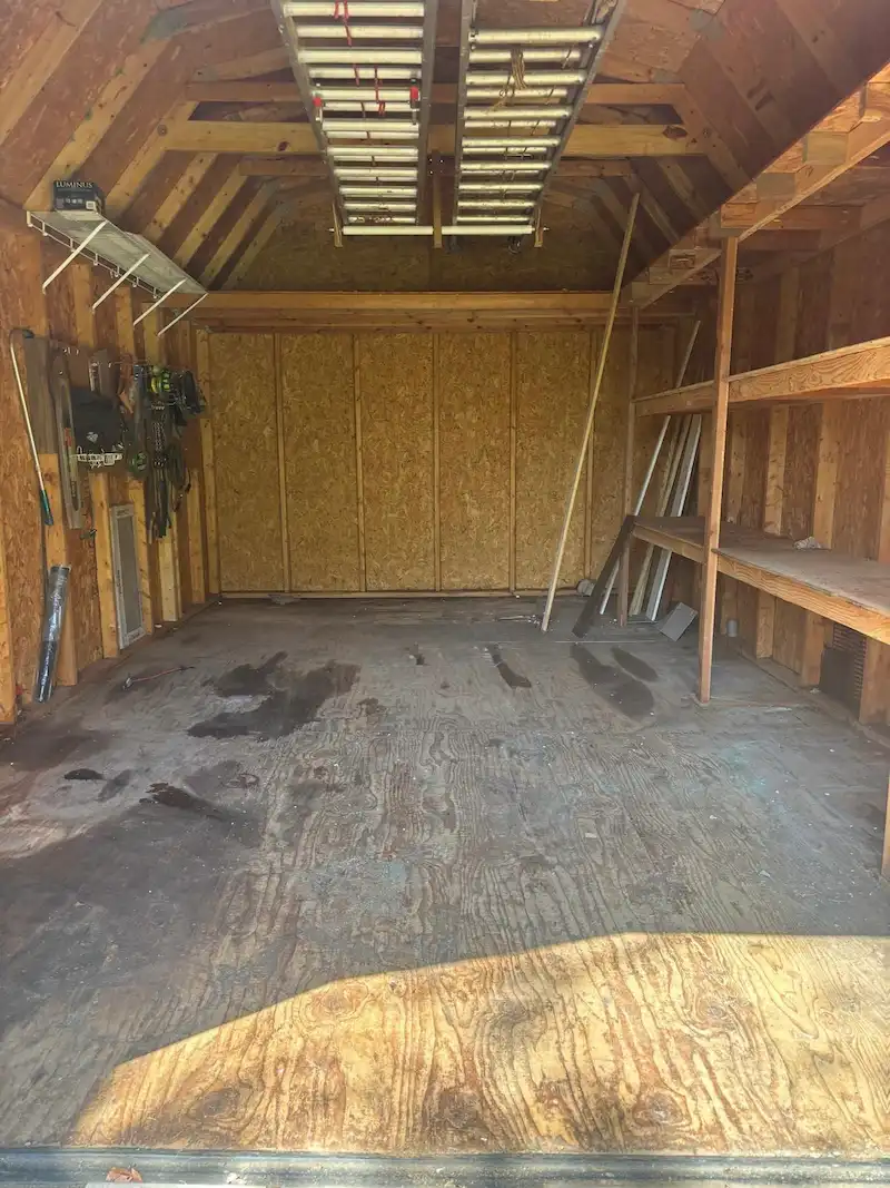 Interior of a New Jersey storage shed cleared of junk and debris by JunkDoctors, showcasing reclaimed floor space while functional items like overhead ladders remain.