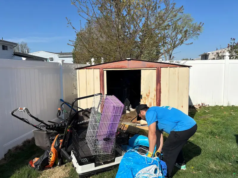 Junk Doctors NJ team member clearing out an old metal shed filled with lawn mowers, cages, and backyard junk in a North NJ residential yard.