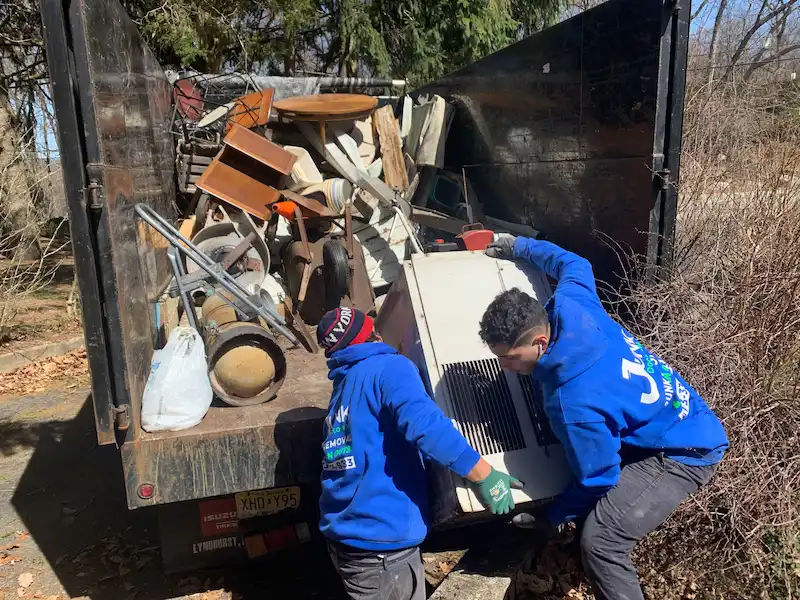 Two crew members lifting an appliance into a junk truck.